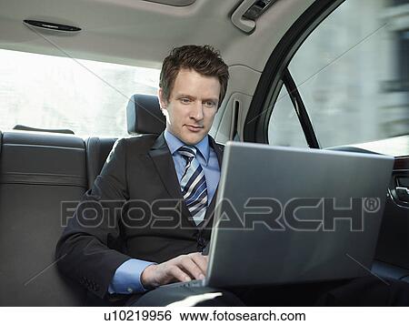 Mid adult businessman sitting at back seat of car using laptop View Large Photo Image Stock Photograph - Mid adult businessman sitting at back seat of car using laptop. Fotosearch