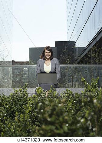 Mid adult businesswoman sitting outside office buildings using laptop View Large Photo Image Stock Image - Mid adult businesswoman sitting outside office buildings using laptop. Fotosearch