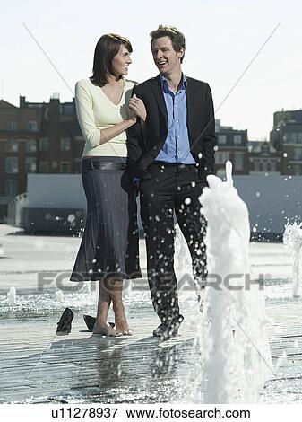 Mid-adult couple standing between water jets of fountain View Large Photo Image Stock Photo - Mid-adult couple standing between water jets of fountain. Fotosearch