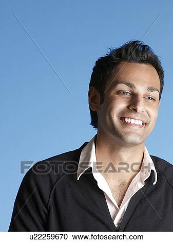 Stock Image - Mid-adult man on blue background looking away and smiling. Fotosearch