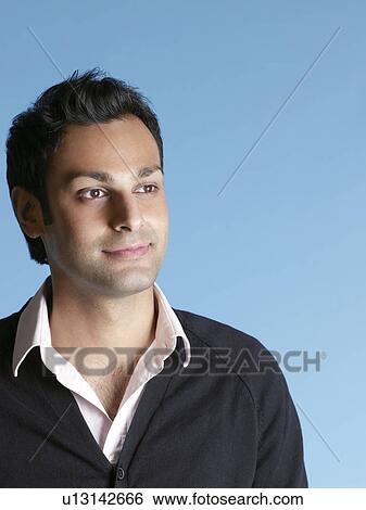 Stock Photograph - Mid adult man on blue background looking away and smiling. Fotosearch