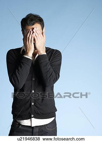 Stock Photo - Mid adult man on blue background with head in hands. Fotosearch