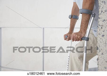 Stock Image - Mid-adult man on crutches mid section side view. Fotosearch