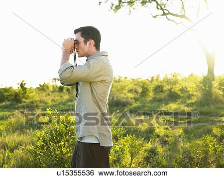 Mid adult man standing in fields looking through binoculars side view View Large Photo Image Stock Photograph - Mid adult man standing in fields looking through binoculars side view. Fotosearch