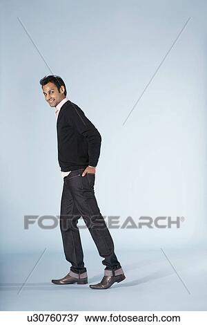 Stock Photo - Mid-adult man walking against blue background side view. Fotosearch