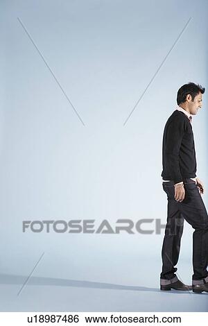 Stock Photograph - Mid-adult man walking against blue background side view (cropped). Fotosearch