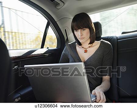 Picture - Mid adult woman at back seat of car using laptop. Fotosearch