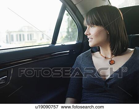 Stock Photo - Mid adult woman at back seat of car looking out window. Fotosearch