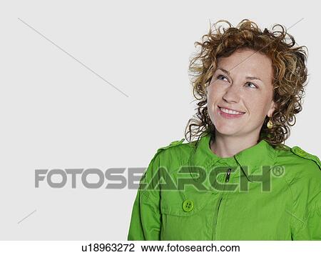 Stock Image - Mid adult woman in green jacket looking up and smiling. Fotosearch