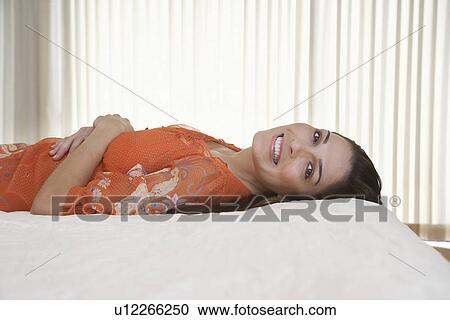 Stock Image - Mid-adult woman lying on bed. Fotosearch
