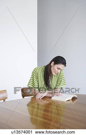 Mid adult woman sitting at table reading book View Large Photo Image Stock Image - Mid adult woman sitting at table reading book. Fotosearch