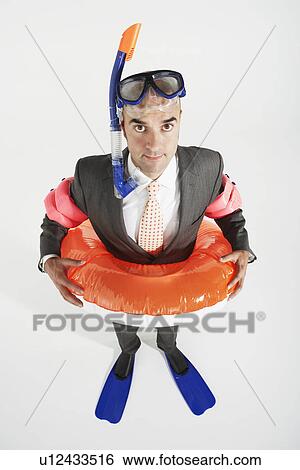 Stock Photograph - Middle-aged businessman in flippers inflatable rubber ring snorkel and goggles. Fotosearch