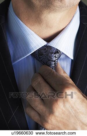 Stock Image - Middle-aged businessman in full suit adjusting tie mid section. Fotosearch