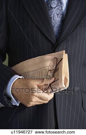 Stock Photo - Middle-aged businessman in full suit holding pair of glasses and newspaper mid section. Fotosearch