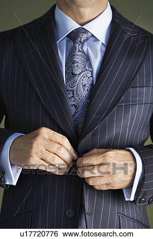 Stock Photograph - Middle-aged businessman in full suit buttoning buttons on jacket mid section. Fotosearch