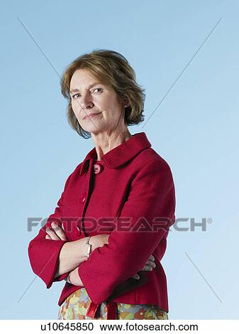Stock Image - Middle-aged woman on blue background arms crossed. Fotosearch