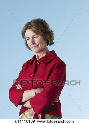 Stock Photo - Middle-aged woman on blue background looking down arms crossed. Fotosearch