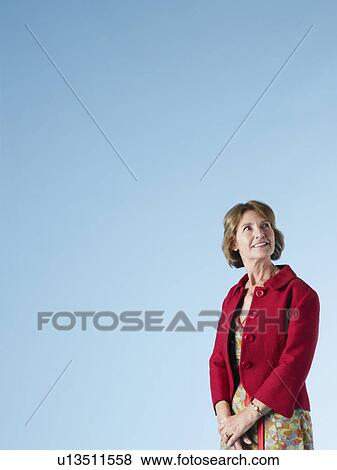 Stock Photo - Middle-aged woman on blue background looking up and smiling. Fotosearch