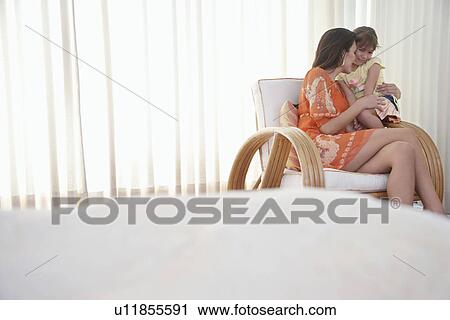 Stock Image - Mother and daughter (5-6) sitting in armchair in bedroom. Fotosearch