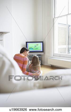 Stock Photograph - Mother and daughter (5-6) watching cartoons in television back view. Fotosearch