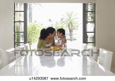 Stock Photo - Mother and daughter (5-6 years) sitting at dining table. Fotosearch
