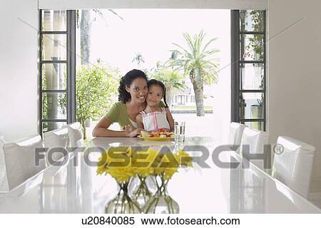 Stock Photography - Mother and daughter (5-6 years) sitting at dining table. Fotosearch