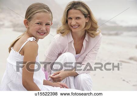Stock Photo - Mother and daughter (7-9) sitting on beach portrait. Fotosearch