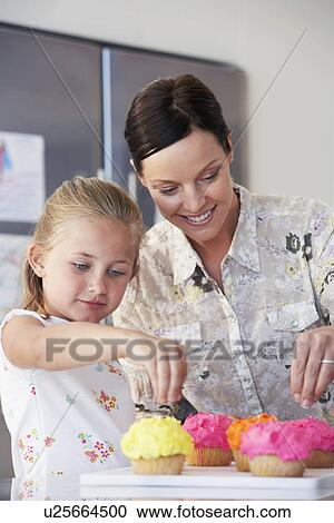 Stock Image - Mother and Daughter Decorating Cupcakes in kitchen. Fotosearch