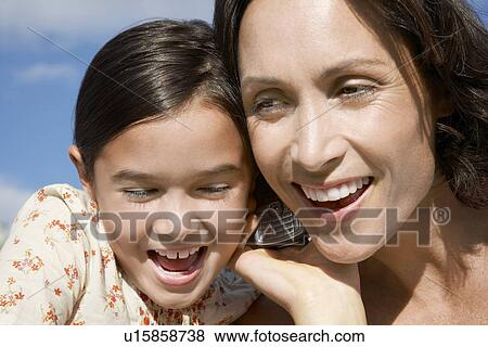 Stock Photo - Mother and daughter heads together using mobile phone head and shoulders. Fotosearch