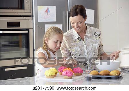 Stock Image - Mother and Daughter Making Cupcakes in kitchen. Fotosearch