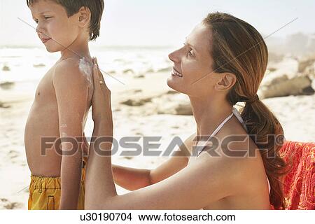 Mother applying protective cream on son's (5-6) back on beach View Large Photo Image Picture - Mother applying protective cream on son's (5-6) back on beach. Fotosearch