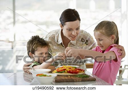 Stock Image - Mother Helping Children Prepare a Meal in kitchen. Fotosearch