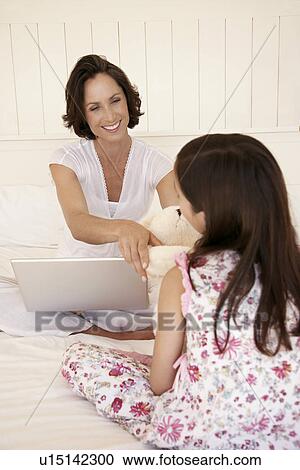 Mother using lap top handing daughter teddy bear sitting on bed View Large Photo Image Stock Image - Mother using lap top handing daughter teddy bear sitting on bed. Fotosearch