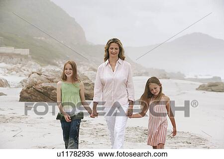 Stock Photography - Mother with two daughters (7-9 10-12) walking on beach. Fotosearch