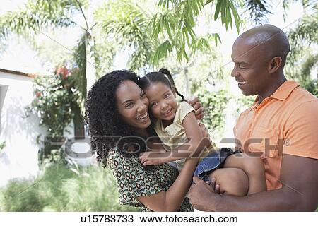 Parents holding daughter (5-6 years) standing in garden View Large Photo Image Stock Image - Parents holding daughter (5-6 years) standing in garden. Fotosearch