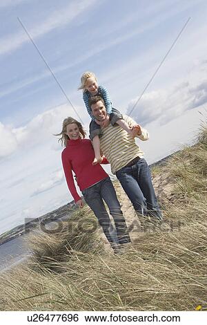 Stock Photograph - Parents walking with girl (5-6) on father's shoulders on dunes portrait. Fotosearch