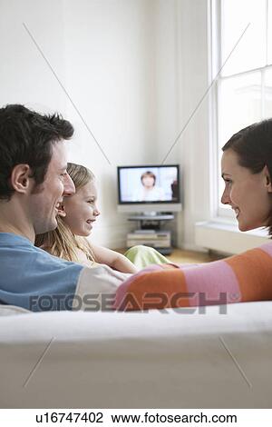 Stock Image - Parents with daughter (5-6) relaxing on sofa in living room. Fotosearch