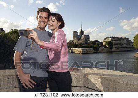 Stock Image - Paris France Couple taking a photo of themselves in front of Notre Dame Cathedral. Fotosearch