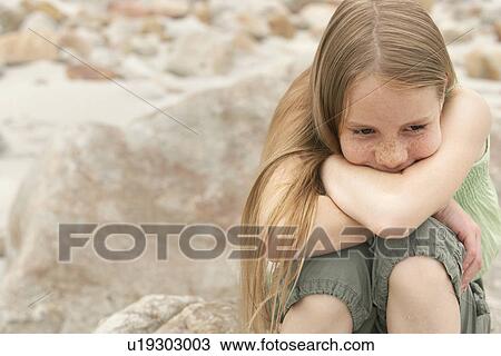 Stock Image - Pensive girl (10-12) sitting on rock on beach. Fotosearch