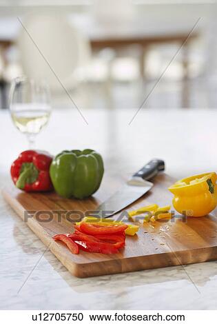 Stock Image - Peppers on chopping board in kitchen. Fotosearch