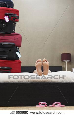 Stock Image - Person lying down in bed next to stack of suitcases. Fotosearch