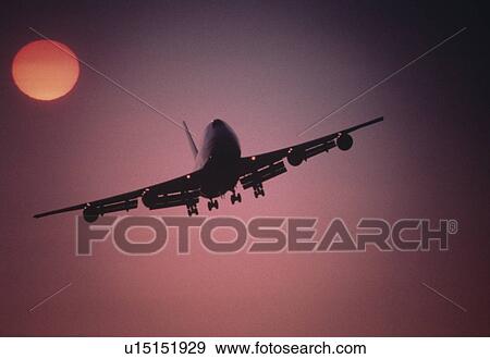 Stock Photo - Plane Flying below setting sun at Sunset. Fotosearch