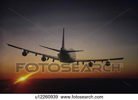 Stock Photo - Plane Flying sun setting on horizon back view. Fotosearch