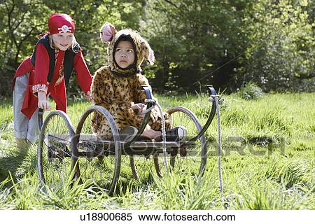 Stock Photography - Portrait of boy (7-9) wearing pirate costume pushing boy (5-6) in cart in jaguar costume garden. Fotosearch