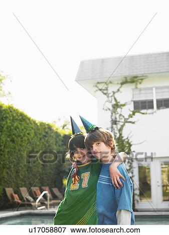 Stock Photo - Portrait of two boys (10-12) in party hats in yard. Fotosearch