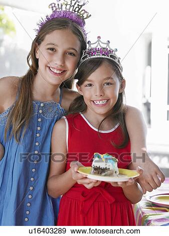 Stock Photo - Portrait of two girls (7-9 10-12) in tiaras one holding plate with cake smiling. Fotosearch