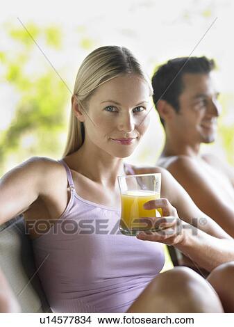 Picture - Portrait of woman holding glass of juice man in background focus on foreground. Fotosearch