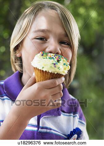 Stock Photograph - Portrait of young boy (7-9) eating cupcake. Fotosearch