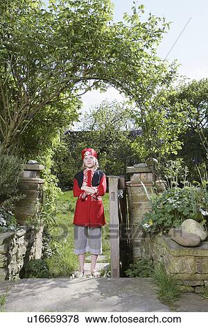 Stock Photo - Portrait of young boy (7-9) wearing pirate costume standing in garden. Fotosearch