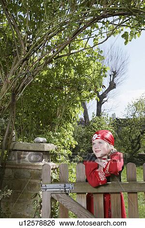 Stock Photograph - Portrait of young boy (7-9) wearing pirate costume leaning on garden gate. Fotosearch